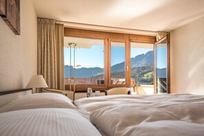 A hotel room with two beds, a desk, a chair, and a large window offering a mountain view. - Seehotel Sternen (Horw)