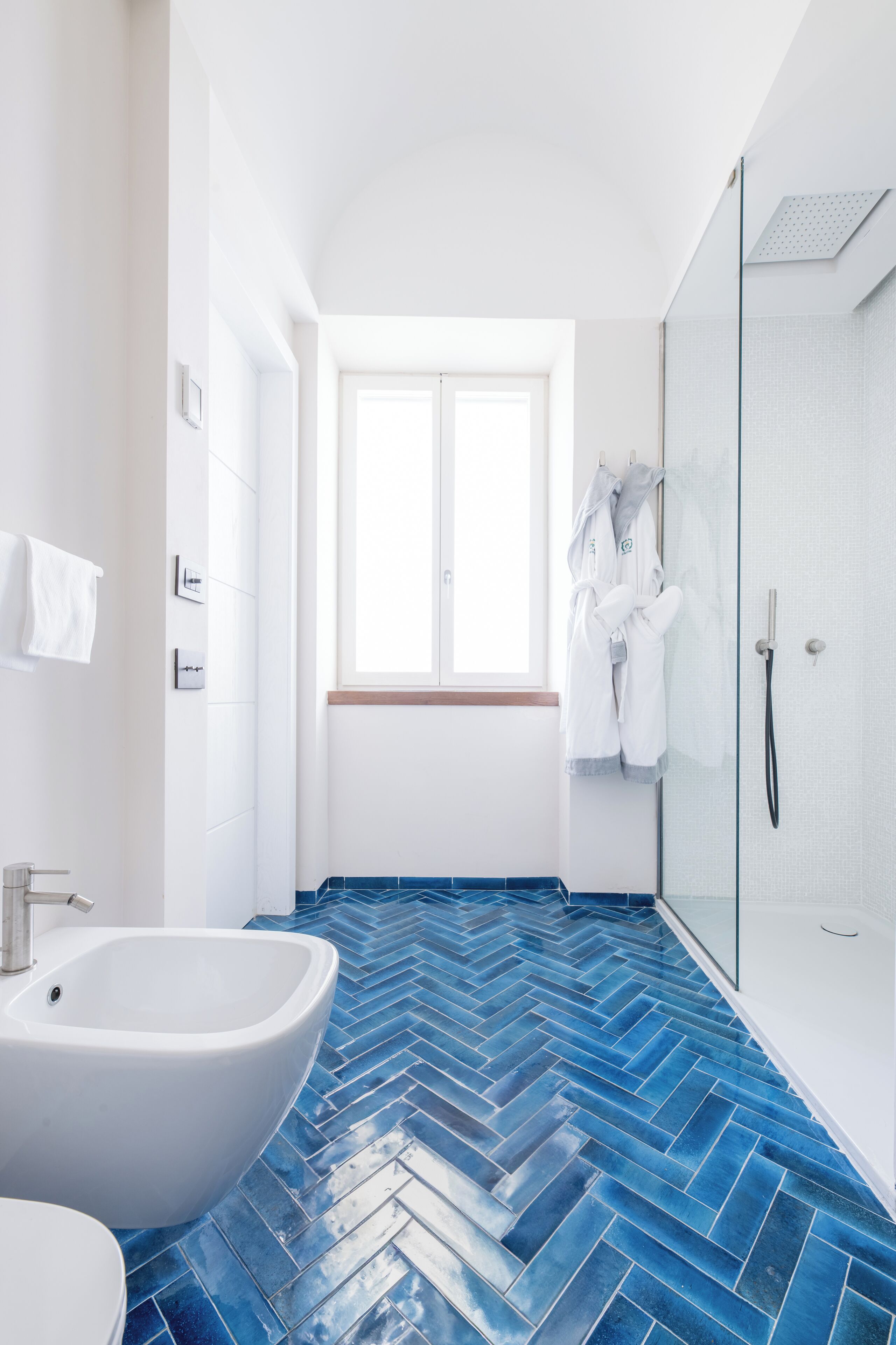 A modern bathroom with a herringbone tile floor, a white sink, and a glass shower enclosure.