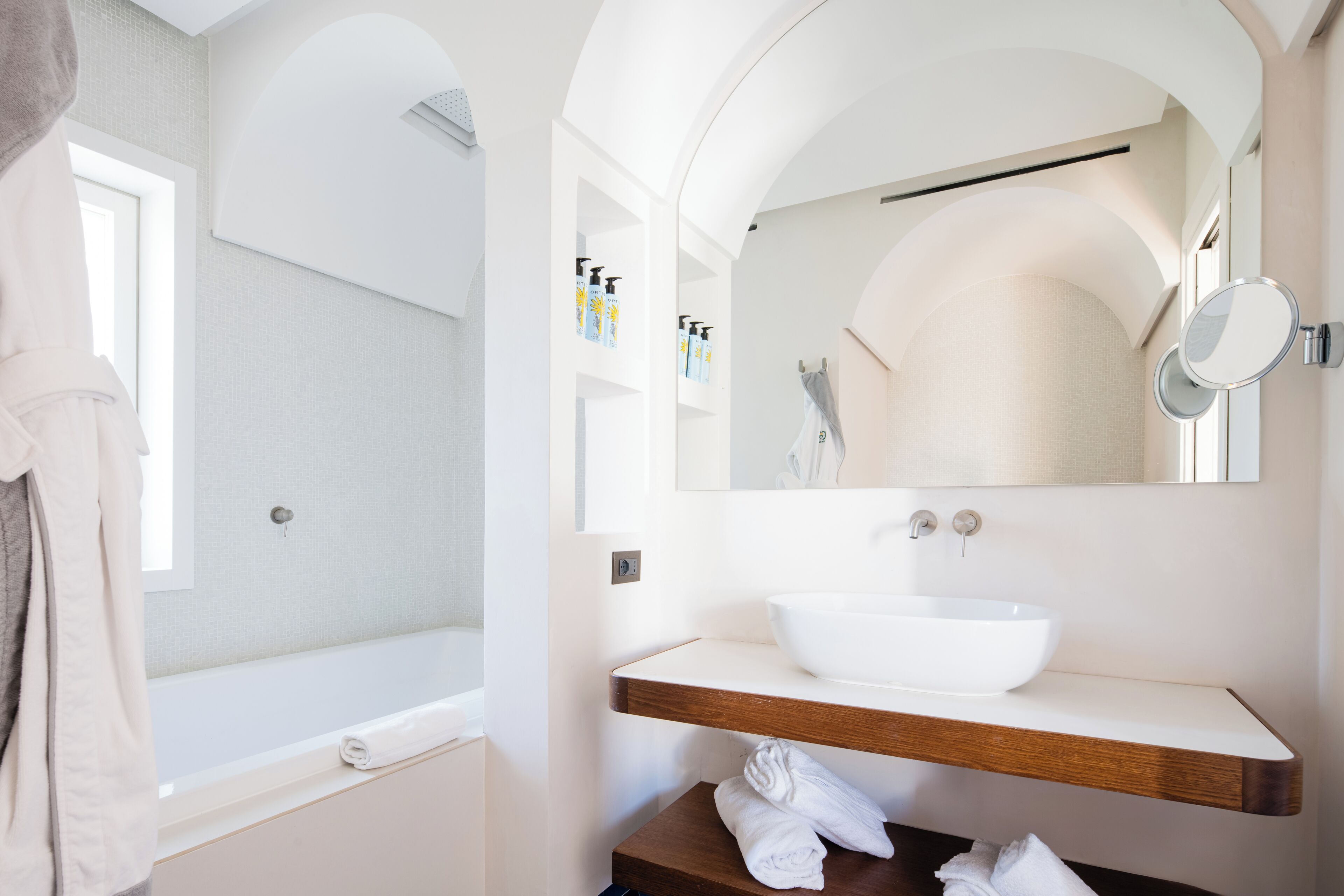 Un baño moderno con una bañera blanca, un mueble de tocador de madera y un lavabo blanco, además de un espejo grande.