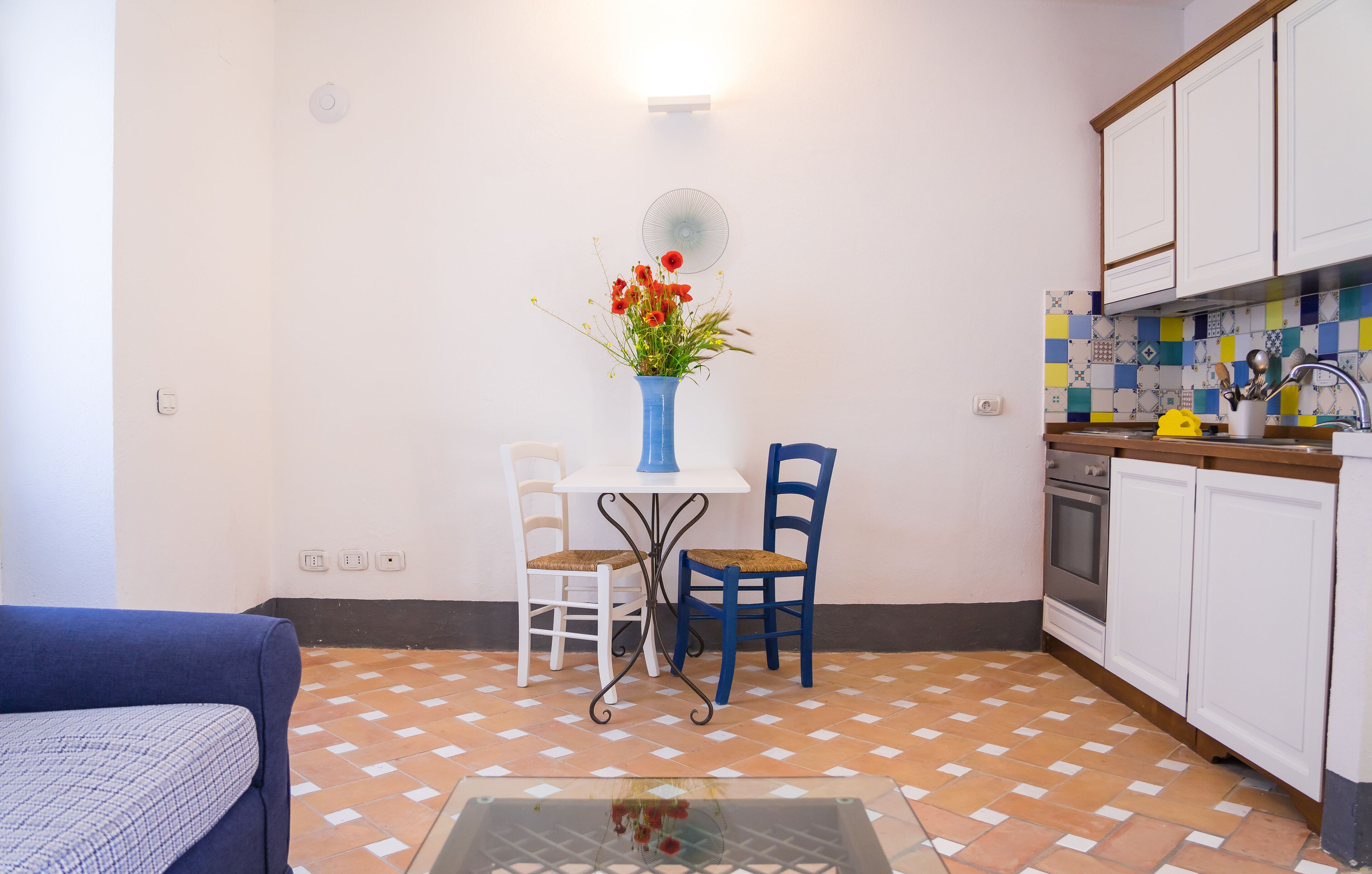 Een compacte keuken met witte kastjes, een betegelde spatwand en een eethoek met een tafel en stoelen.