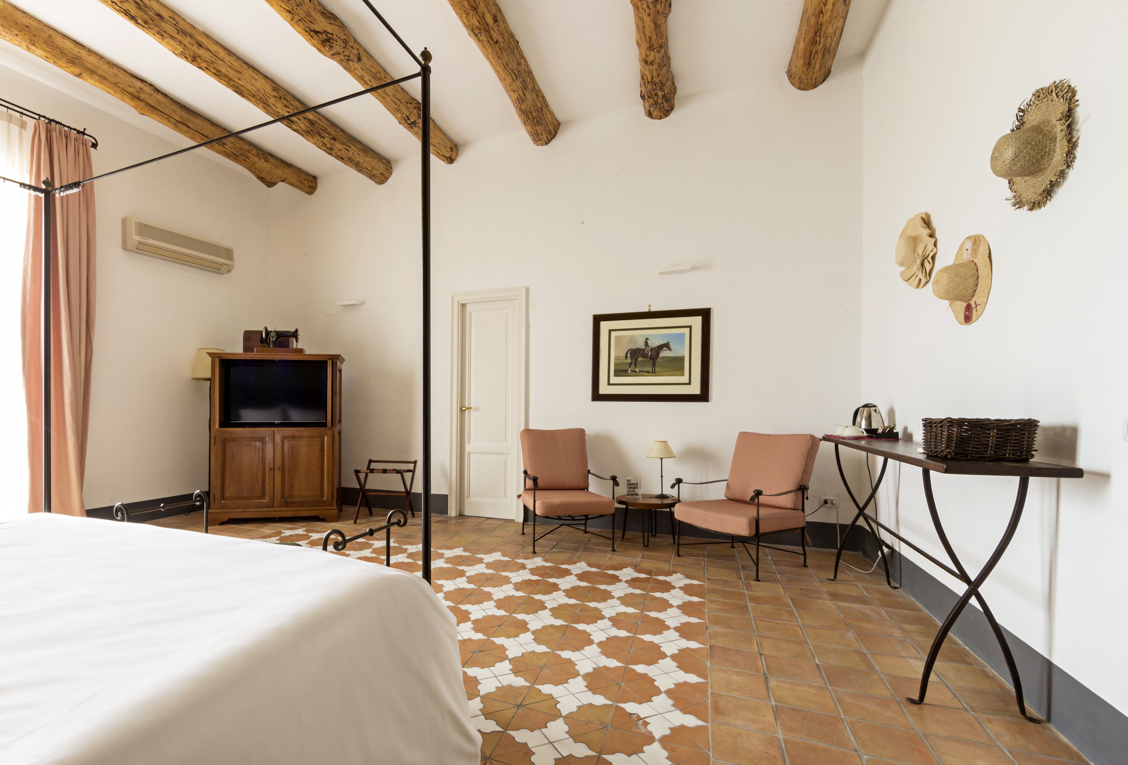 A hotel room with a bed, two chairs, a table, a television, and a patterned floor.