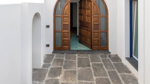 Un edificio blanco con un patio empedrado de piedra, una puerta de madera y un ventanal pequeño.