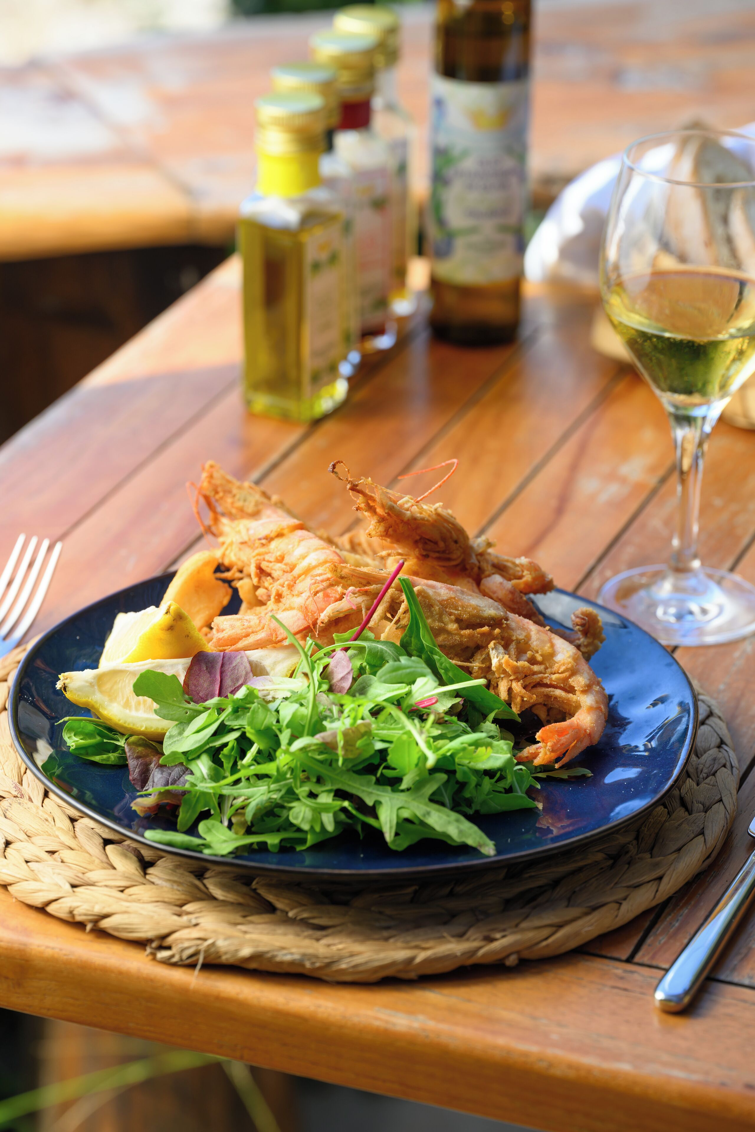 A table with a plate of food, a glass of wine, and bottles of olive oil.