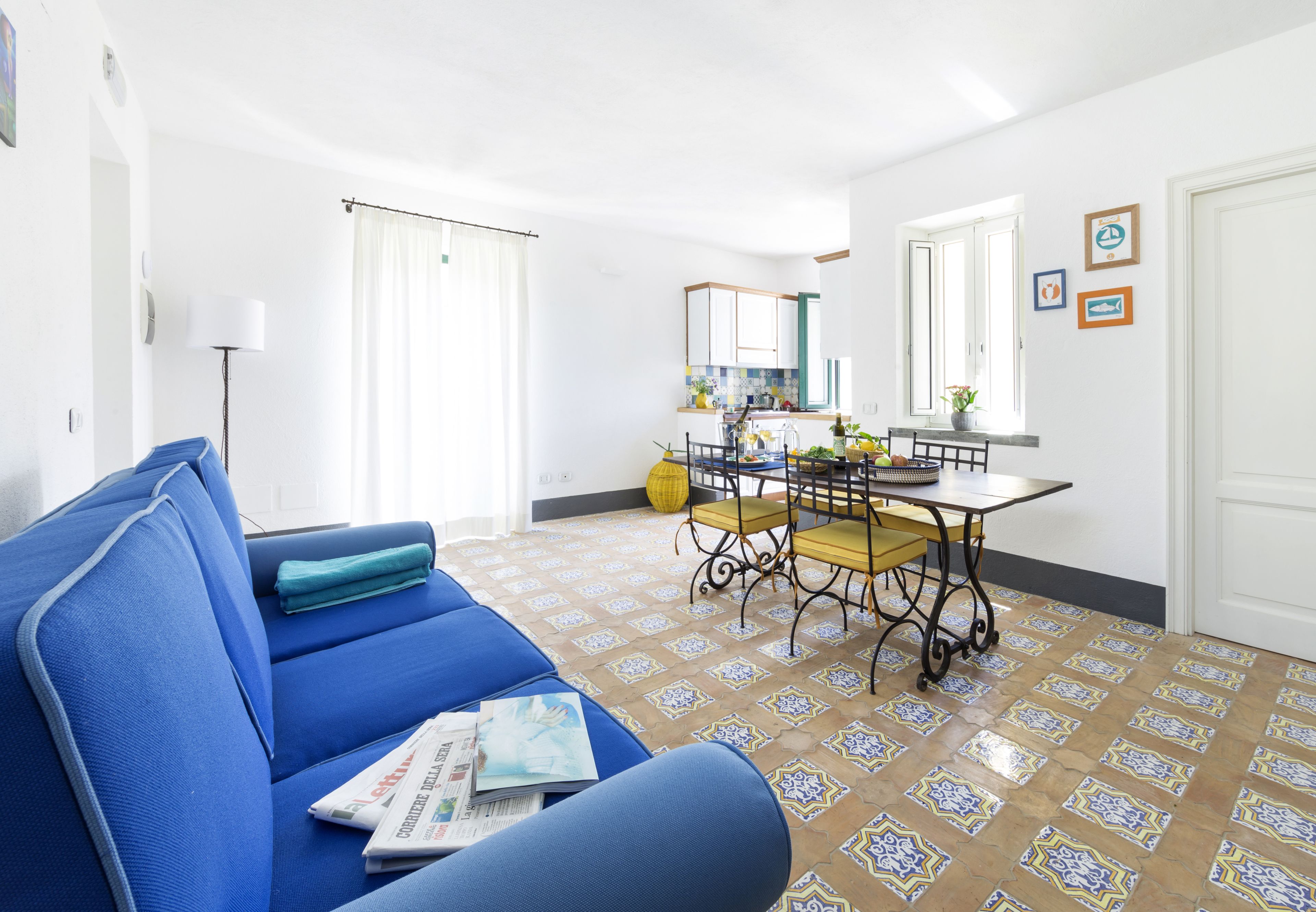 Sala de estar com sofá azul, mesa de jantar com cadeiras e área de cozinha ao fundo.