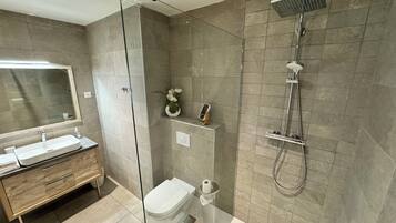 Un baño moderno con ducha envuelta en vidrio, tocador con espejo y un inodoro.