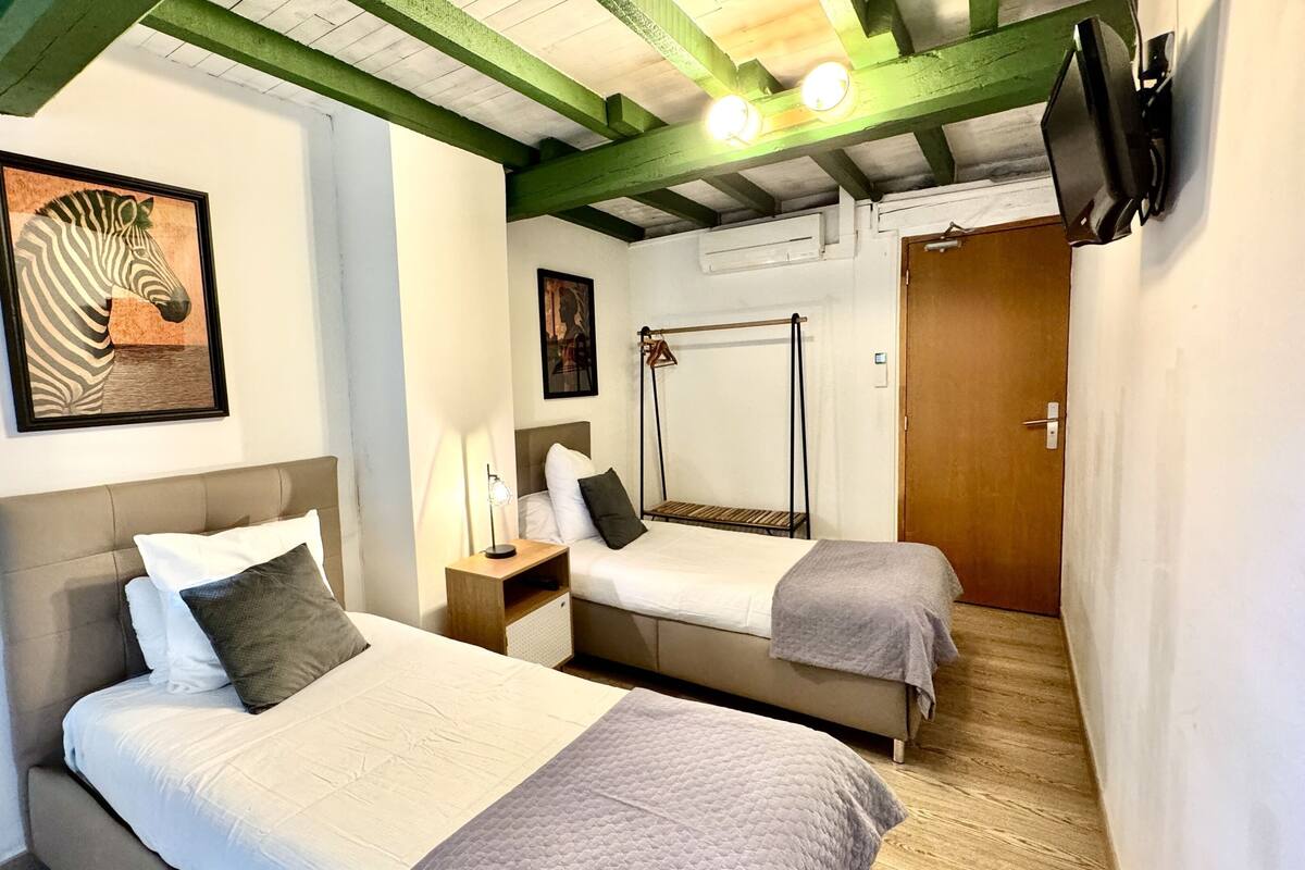 A room with two beds, a wooden floor, a zebra painting, and a wooden door.