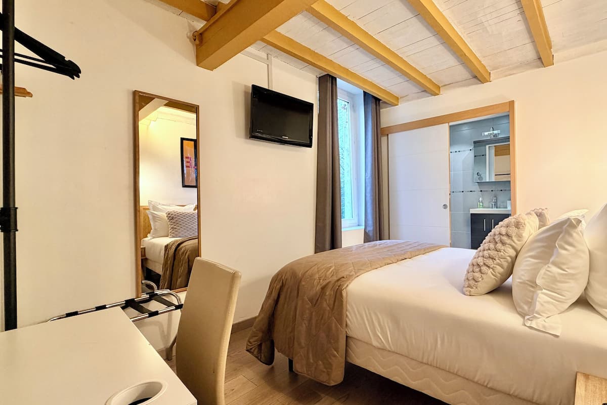 A hotel room with a bed, a desk, a chair, a television, and a window.