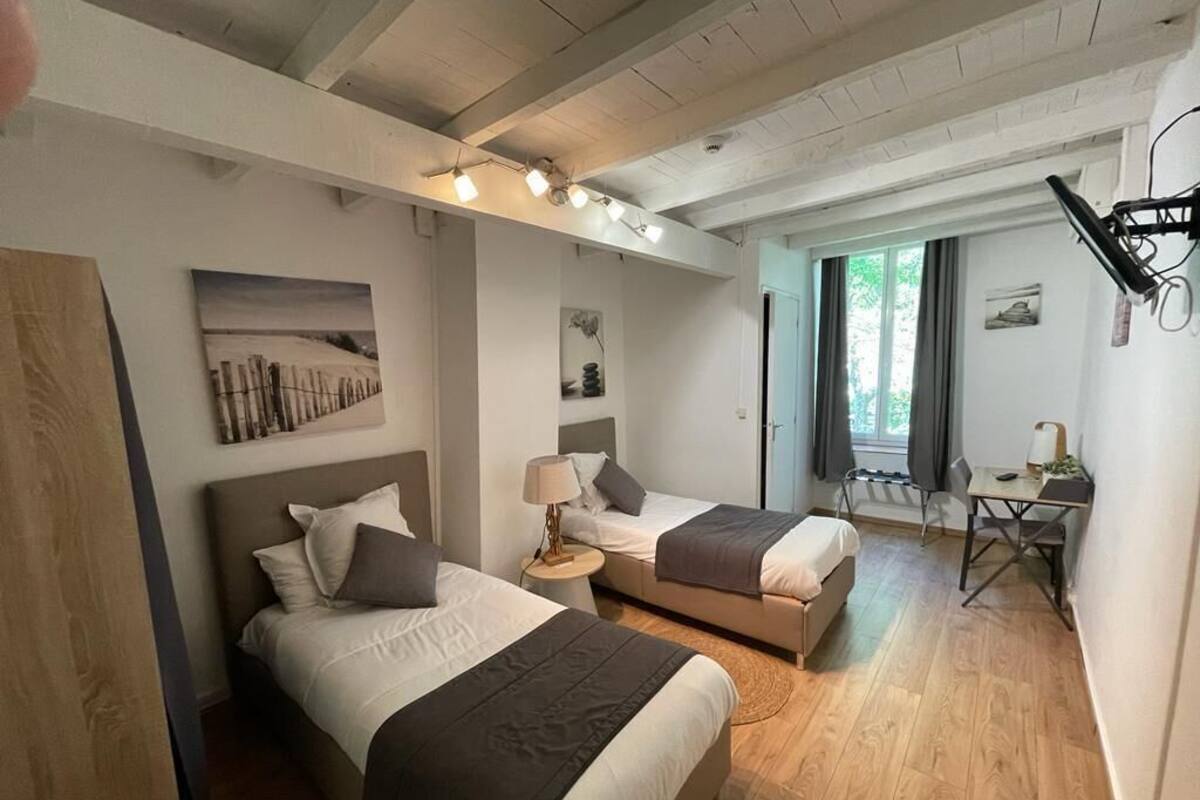 A hotel room with two beds, a desk, a chair, and a window.