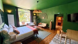 A room with a bed, a sofa, a small table, a lamp, a hanging light fixture, a potted plant, and a view of the outdoors. - Hôtel le Galambre (Nîmes)