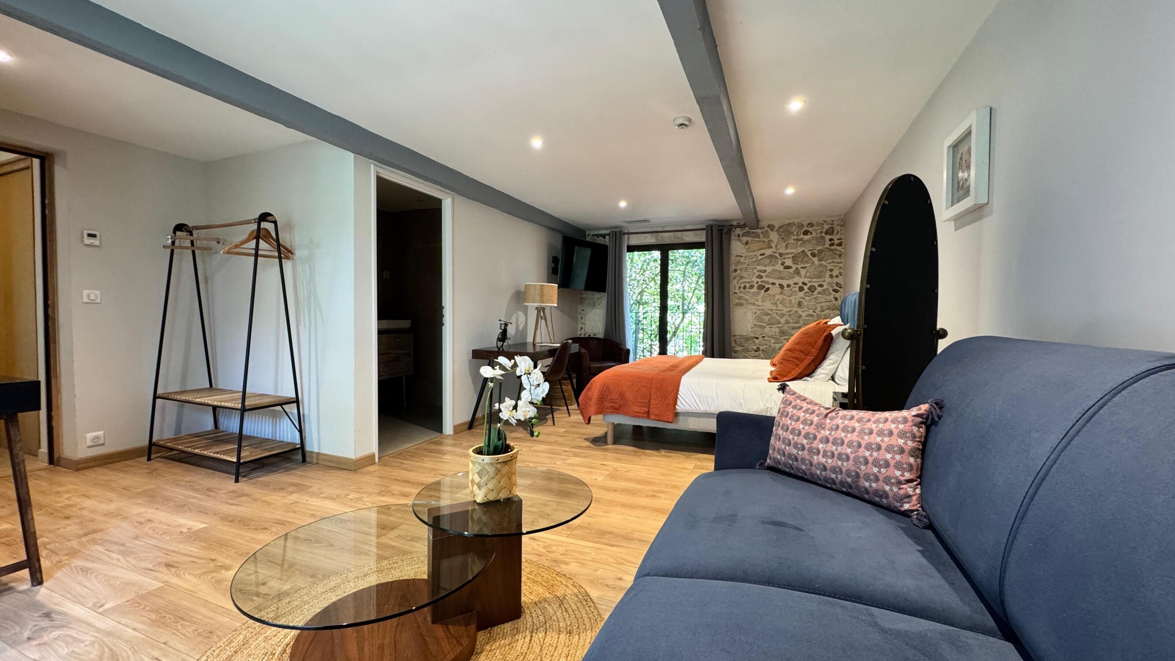 Een moderne kamer met een bed, een slaapbank, een glazen salontafel, een bureau en een hangstoel.