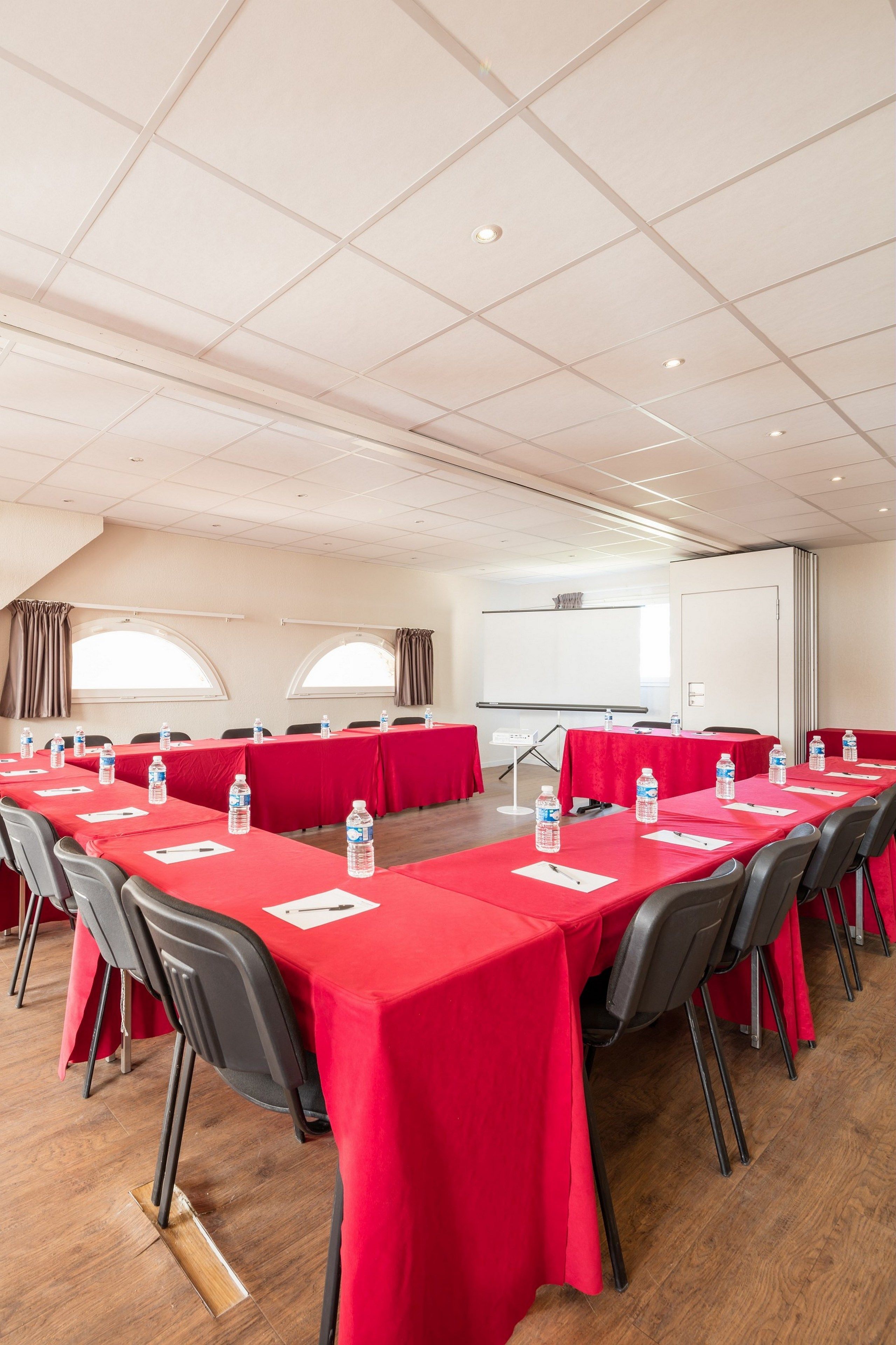A conference room with long tables, chairs, and a projector screen.