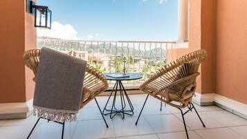 Een balkon met twee rieten stoelen en een kleine ronde tafel, met uitzicht op een schilderachtig stadsbeeld en glooiende heuvels.