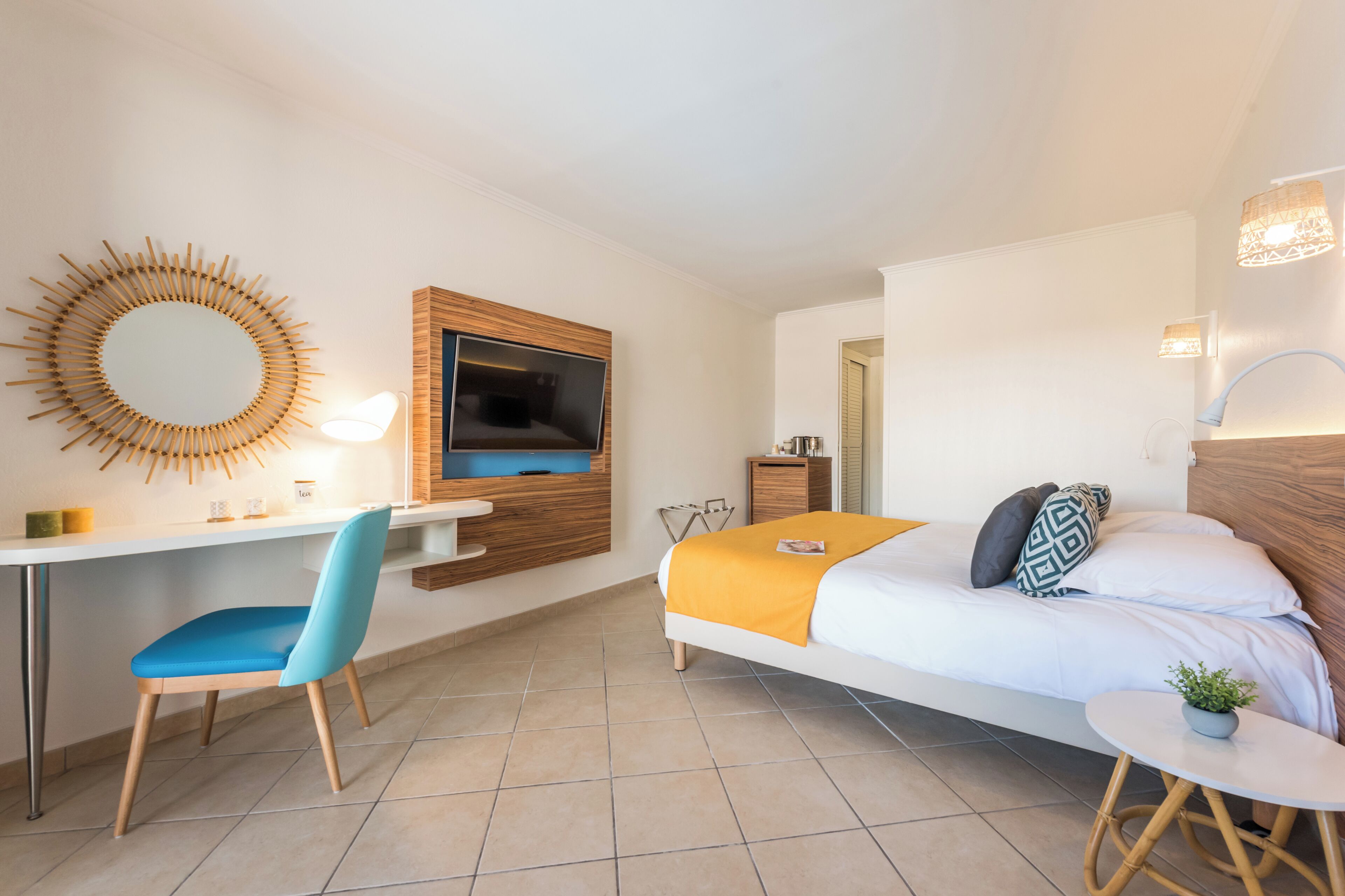 A modern hotel room with a bed, desk, chair, TV, and a small table with a plant.