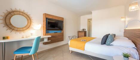 A modern hotel room with a bed, desk, chair, TV, and a small table with a plant.