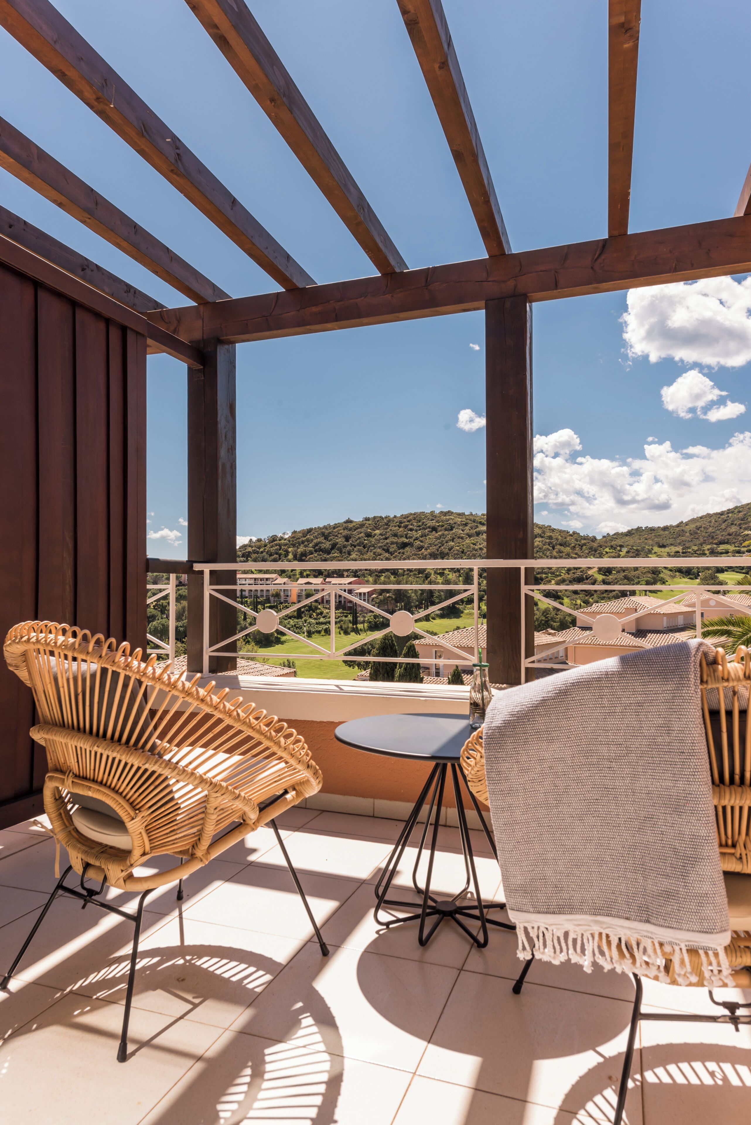 A balcony with wicker chairs, a small table, and a view of a green landscape.