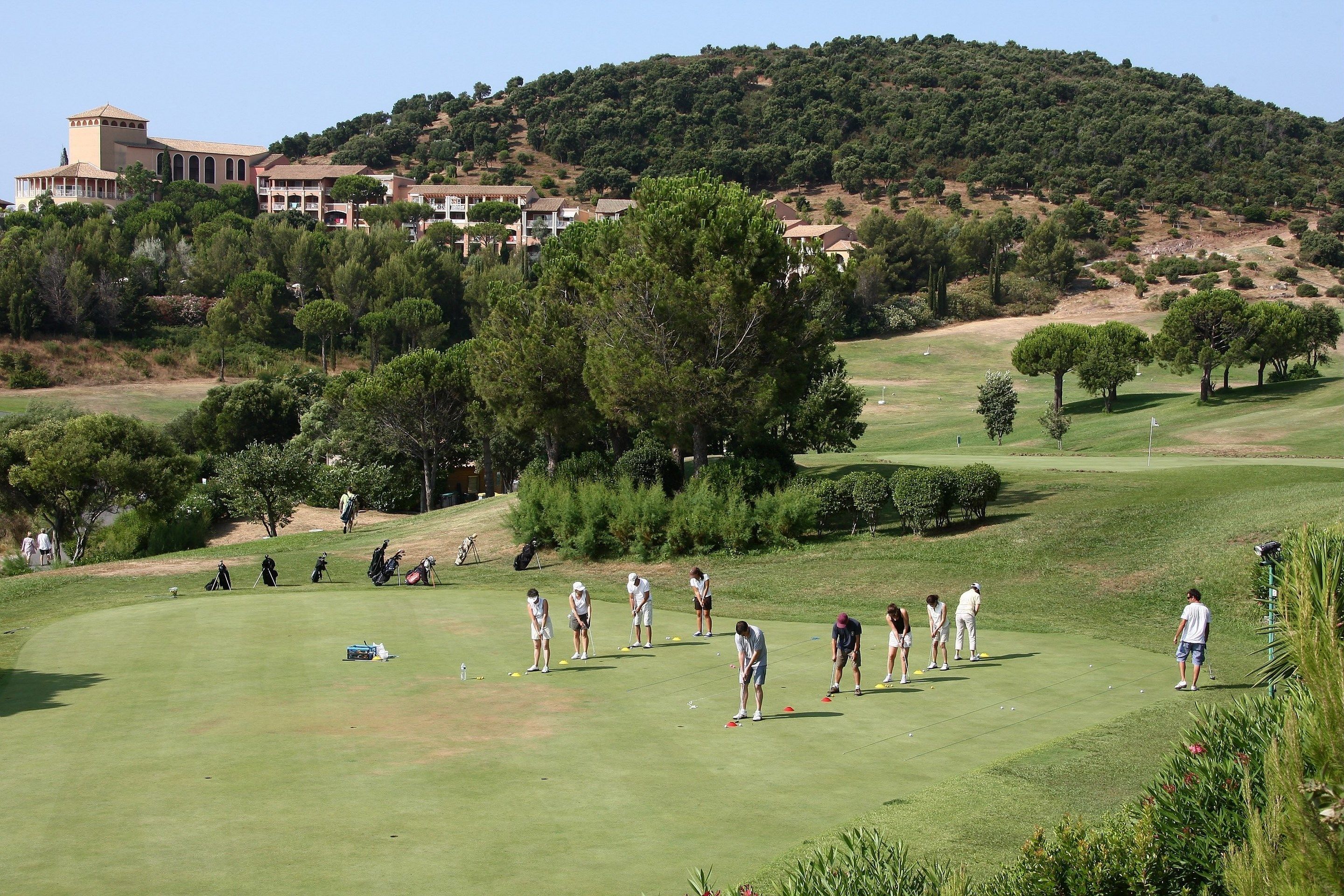 A golf course with players, a clubhouse, and a hill with trees in the background.