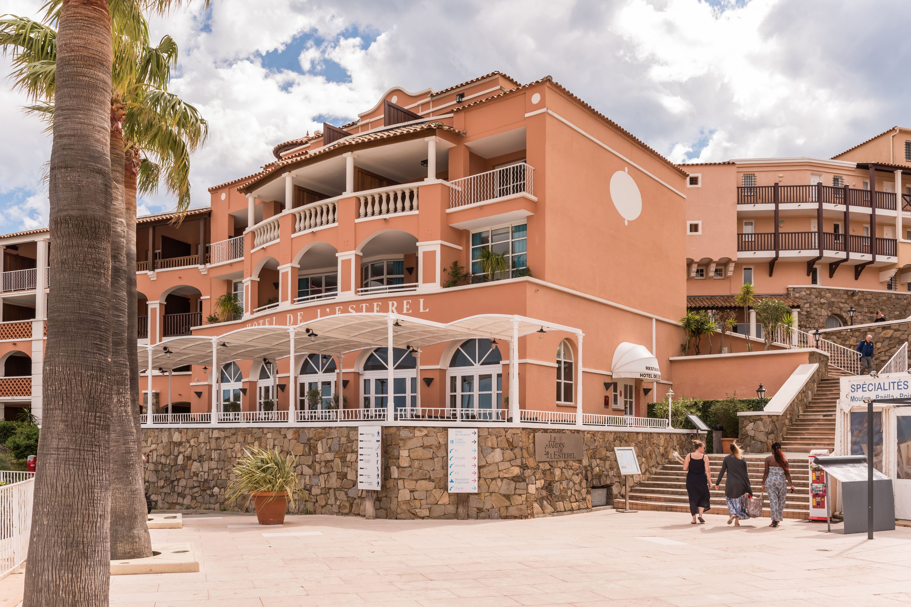 Ein mehrstöckiges Hotel mit Balkonen, einer überdachten Eingangsparte und einer Steinmauer.