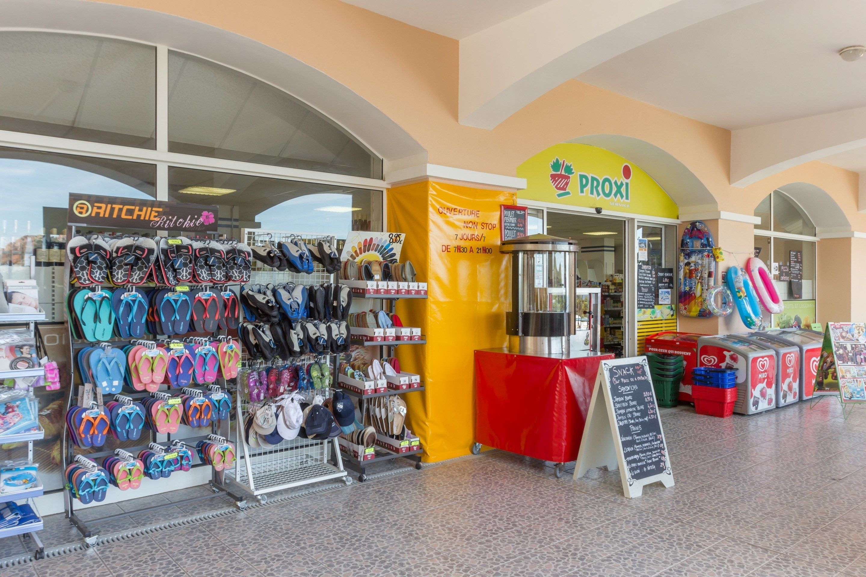A store with flip-flops and sandals on display, a coffee shop, and a kiosk with a sign.