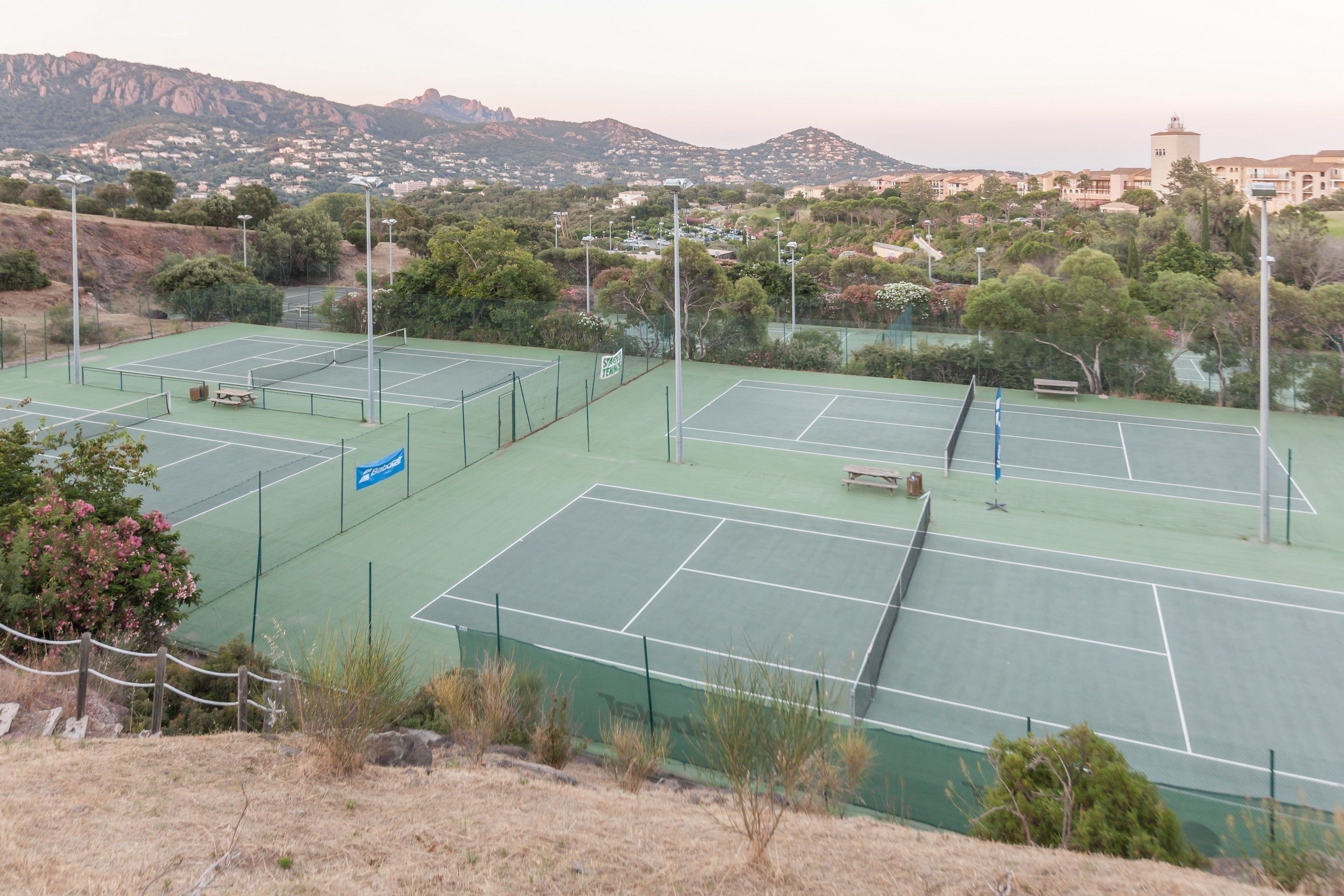 Un complejo de canchas de tenis con varias canchas, rodeado de árboles y edificios residenciales al fondo.