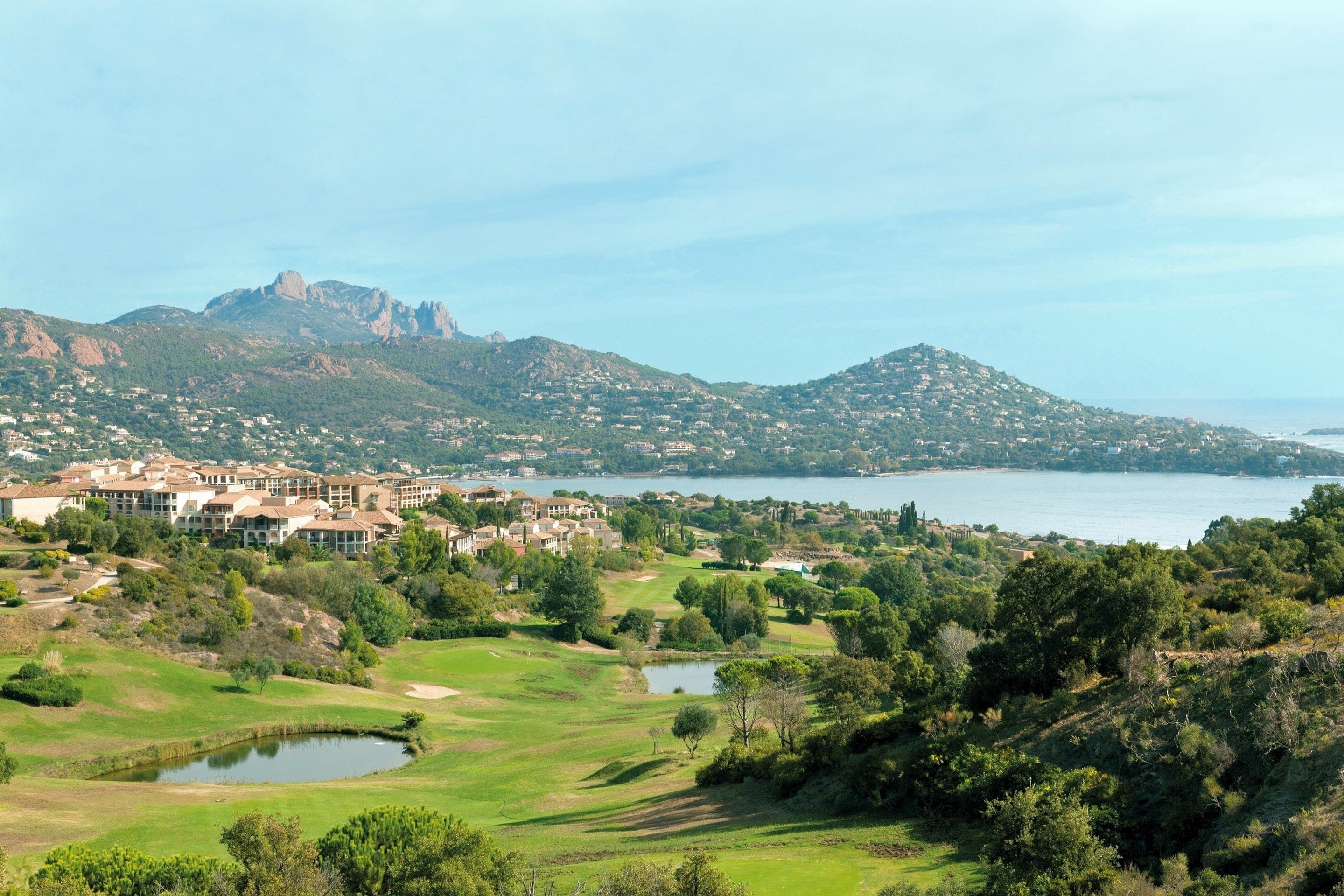 A golf course with a lake, mountains, and a residential area in the background.