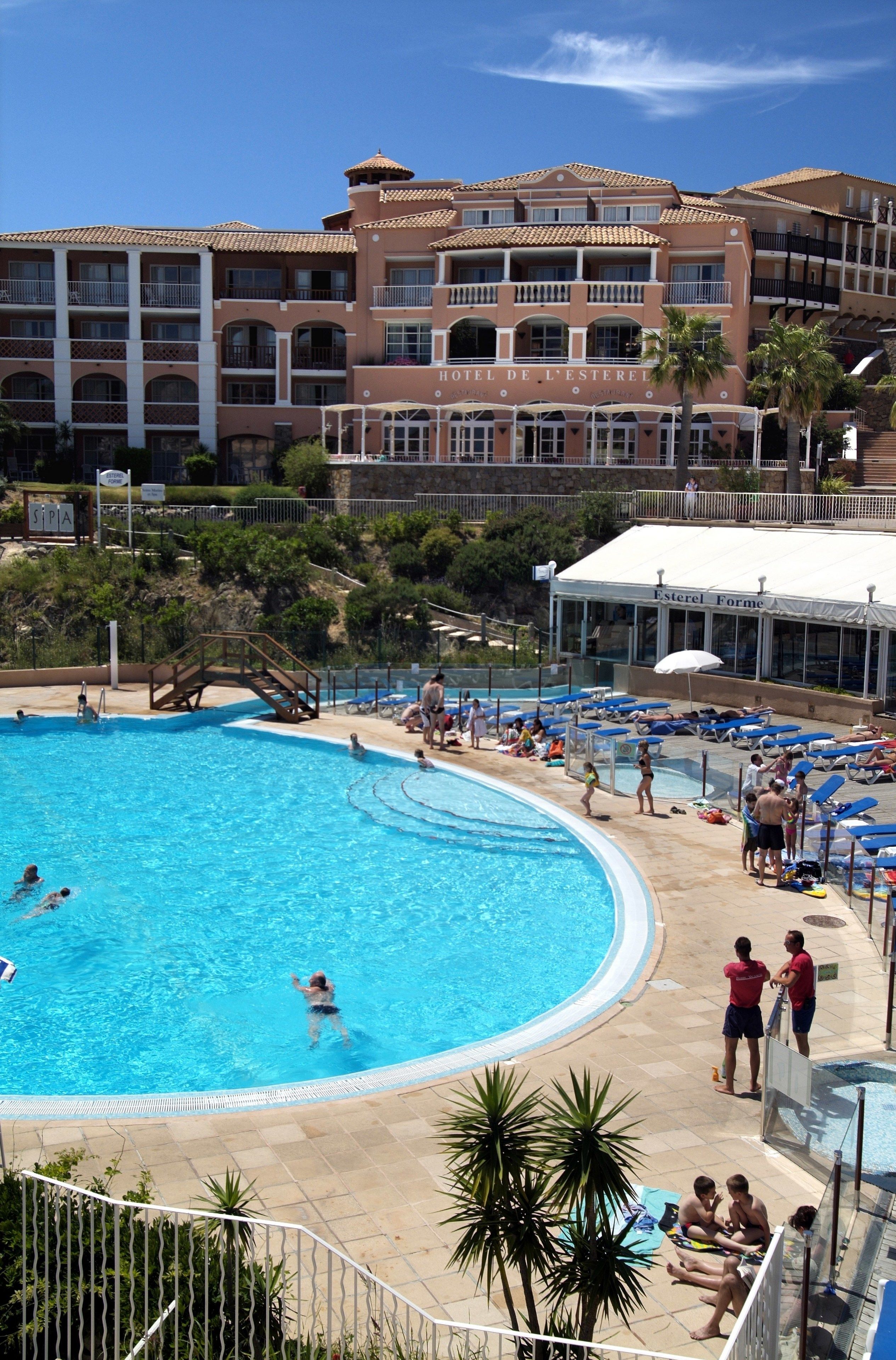 Et hotel med swimmingpool, flere balkoner og et overdækket område med parasoller.