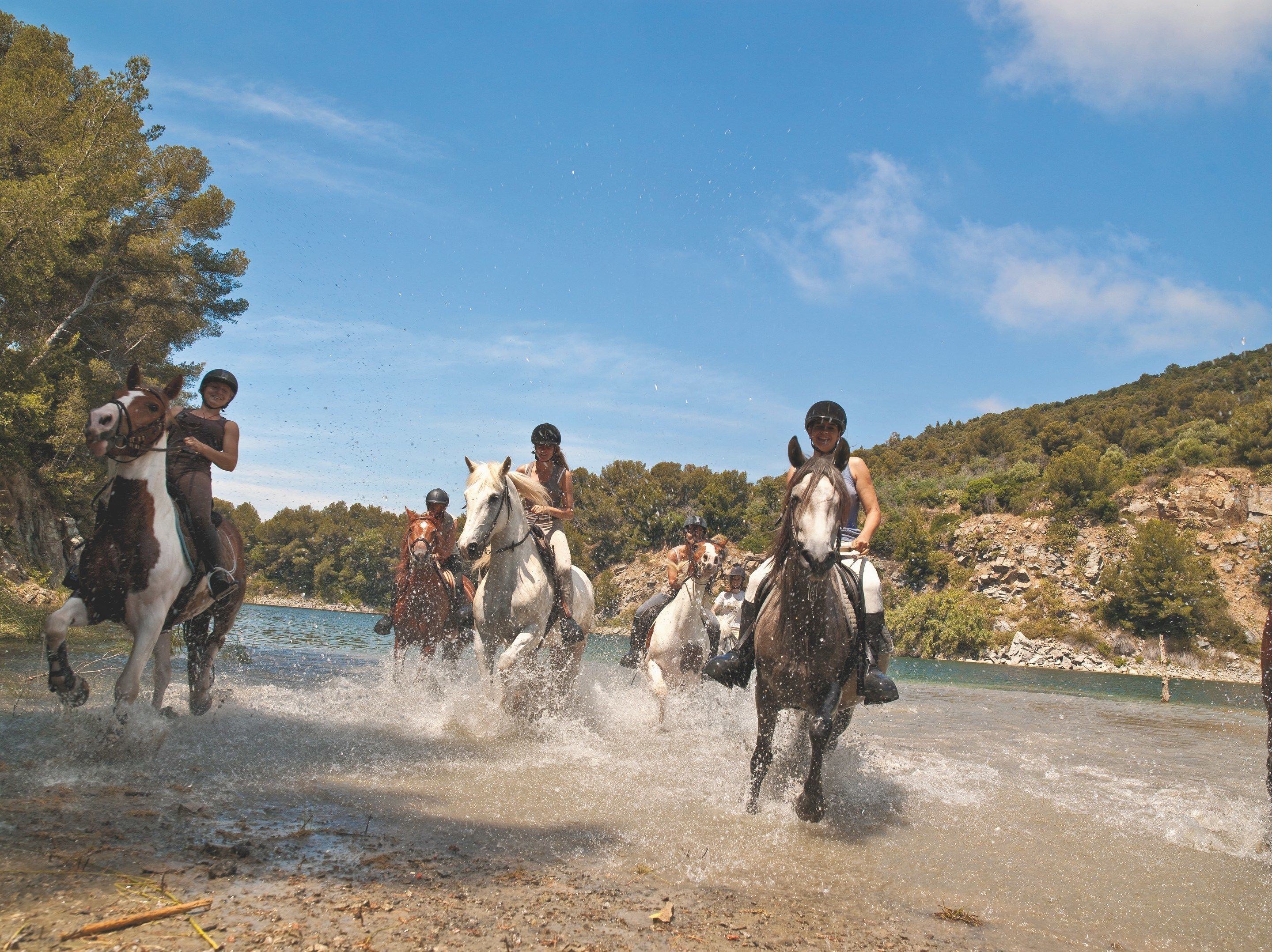 A group of people riding horses along a riverbank.