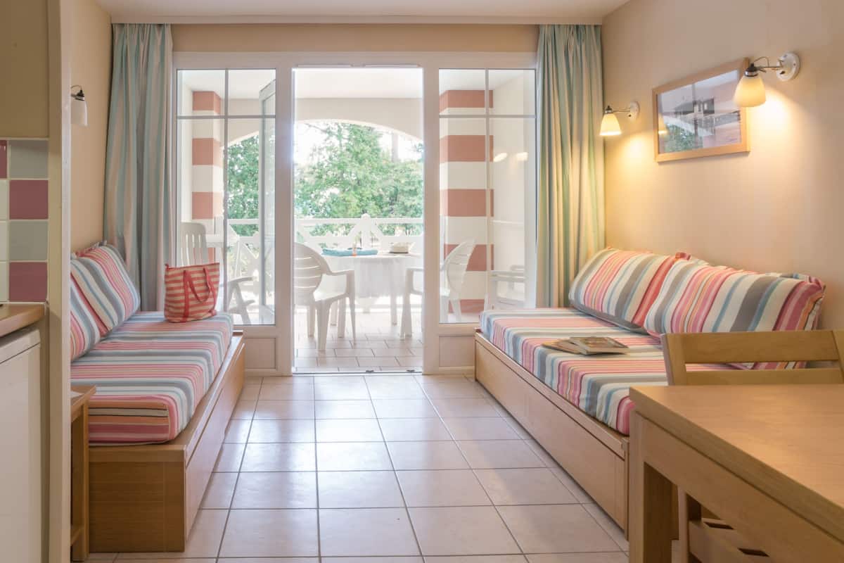 Ein gemütliches Zimmer mit einer Couch und einem Tisch, eine Glastür, die zu einem Außenbereich mit Stühlen führt.