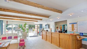 Un espace d’accueil avec un bureau en bois, un coin salon agrémenté de coussins colorés et une grande fenêtre donnant sur l’extérieur.
