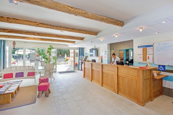 Un área de recepción con un mostrador de madera, una sala de estar con cojines de colores y un ventanal con vistas al exterior.