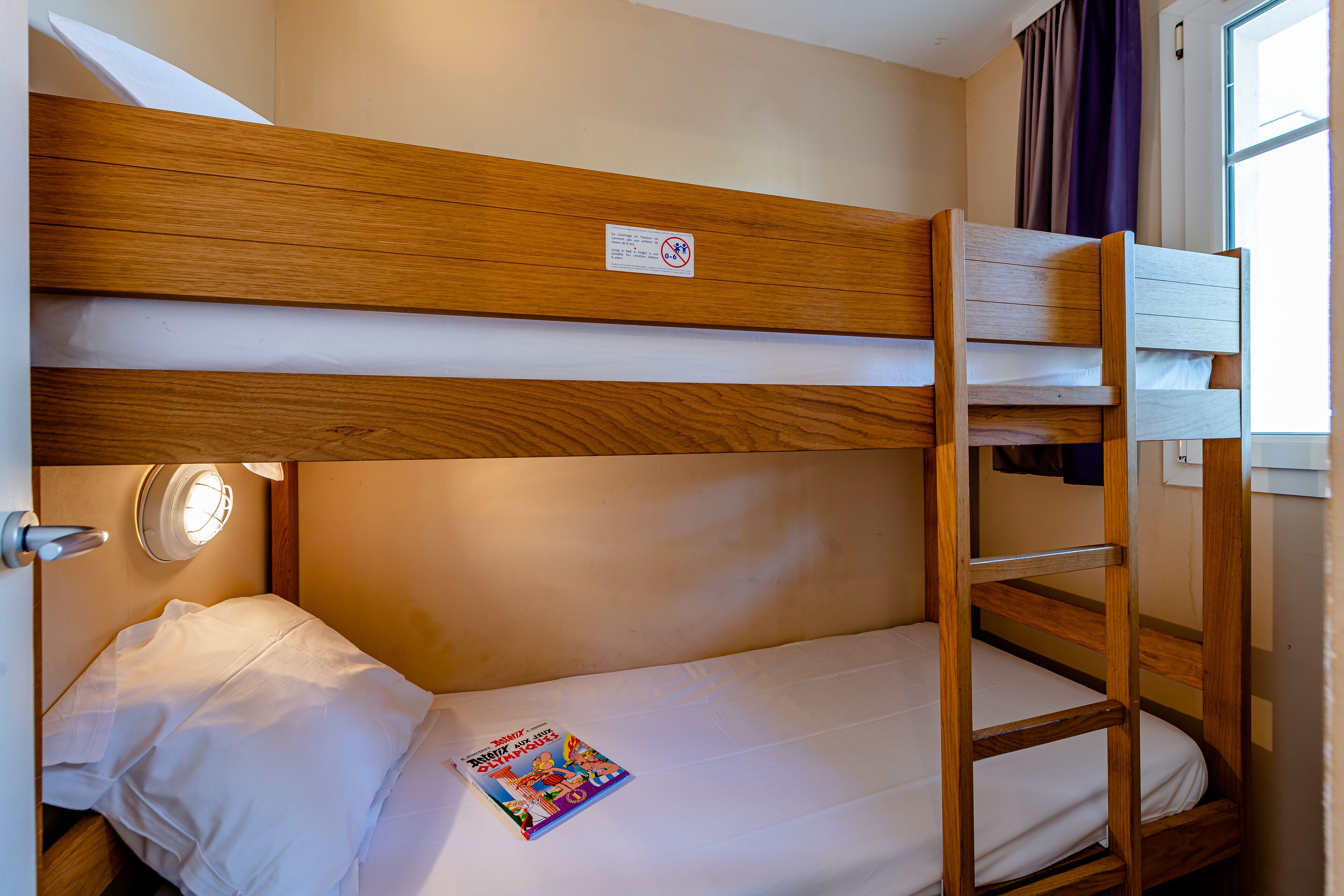 Un lit superposé avec une tête de lit en bois, un matelas blanc et un magazine sur le lit.