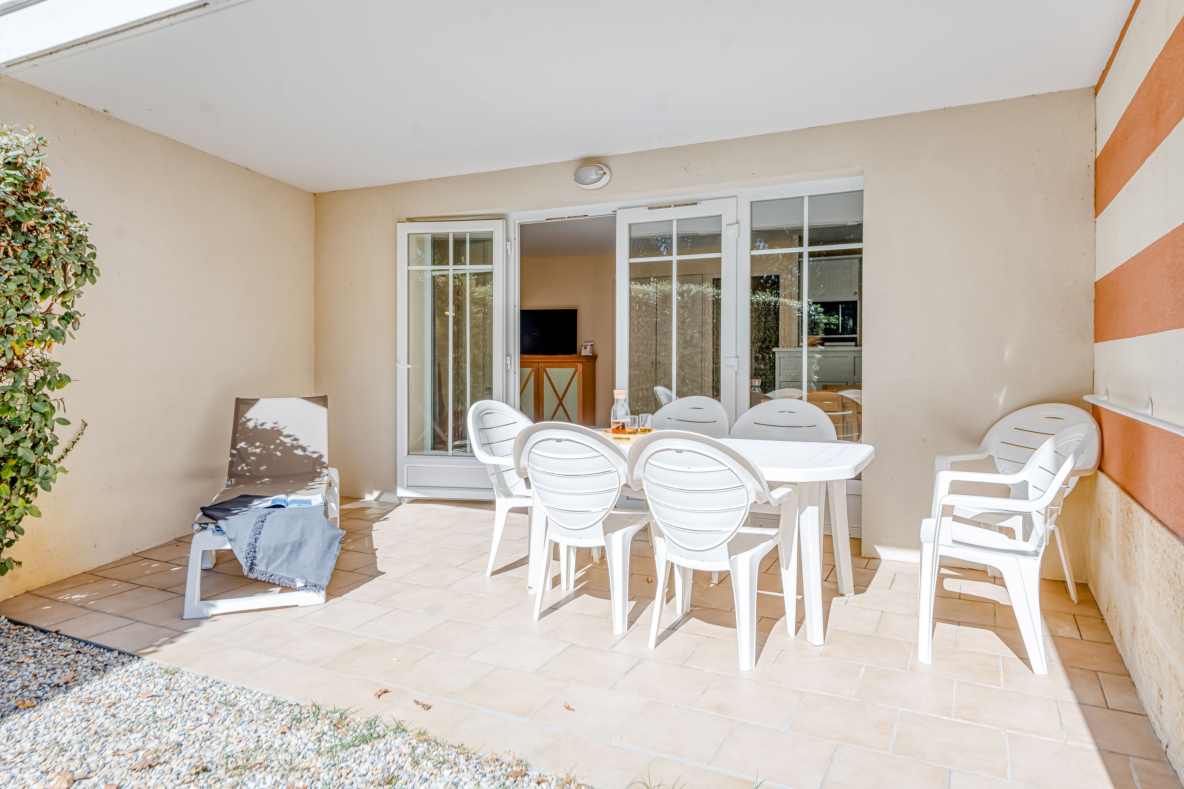 A patio with a table and chairs, a covered seating area, and a sliding glass door leading to a garden.