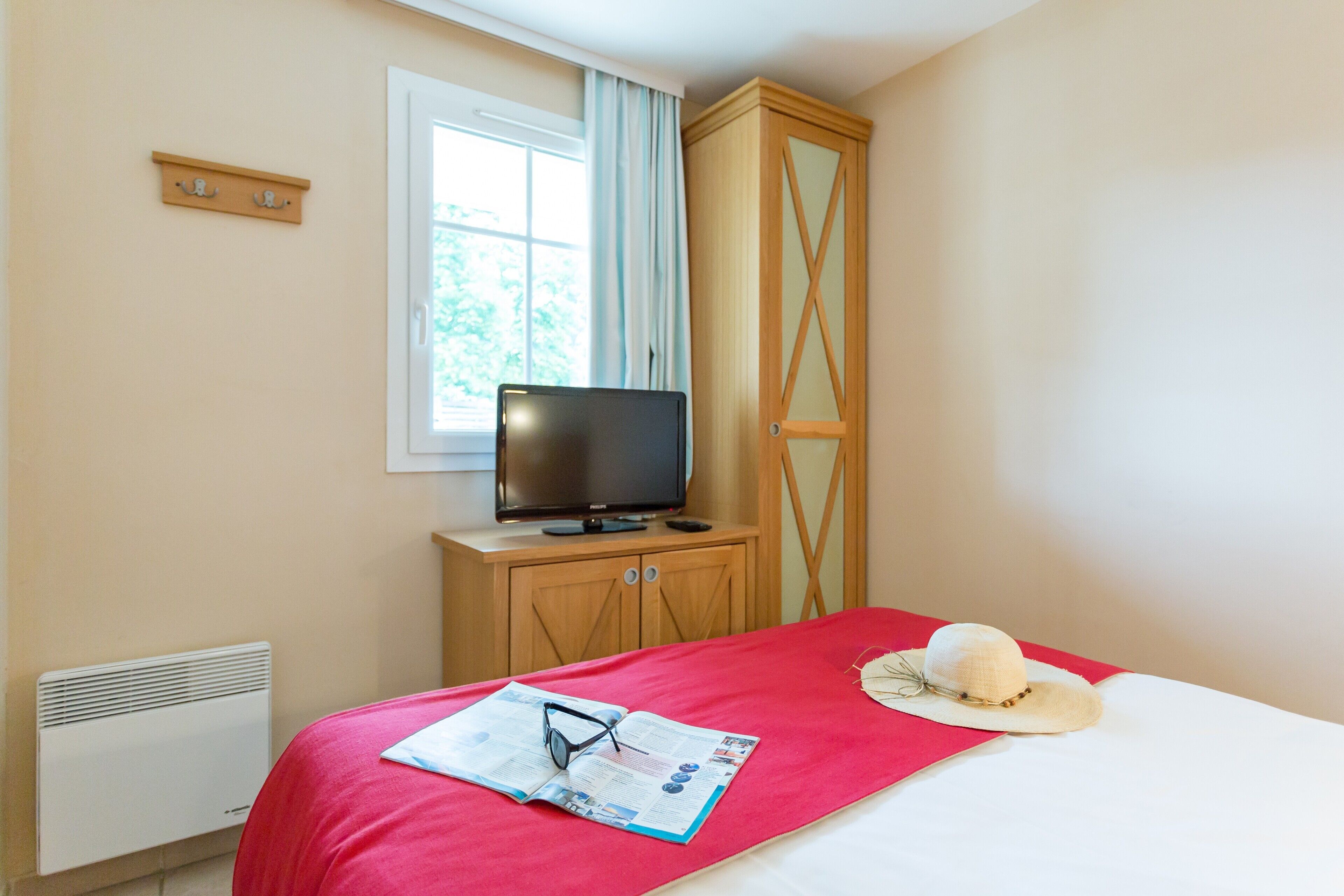 A bedroom with a bed, a television on a wooden cabinet, a window with curtains, and a radiator.