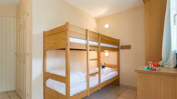A bunk bed with a wooden frame and white bedding, a small bedside table with toys, and a light fixture above the bed.