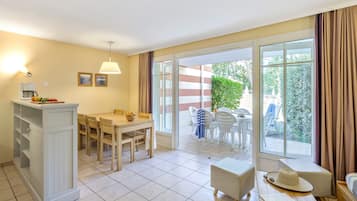 Een lichte kamer met een eettafel, stoelen, een bank en een raam met gordijnen.