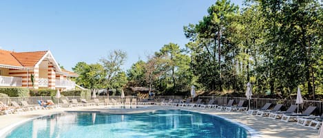 A swimming pool with lounge chairs and a building with a tiled roof.