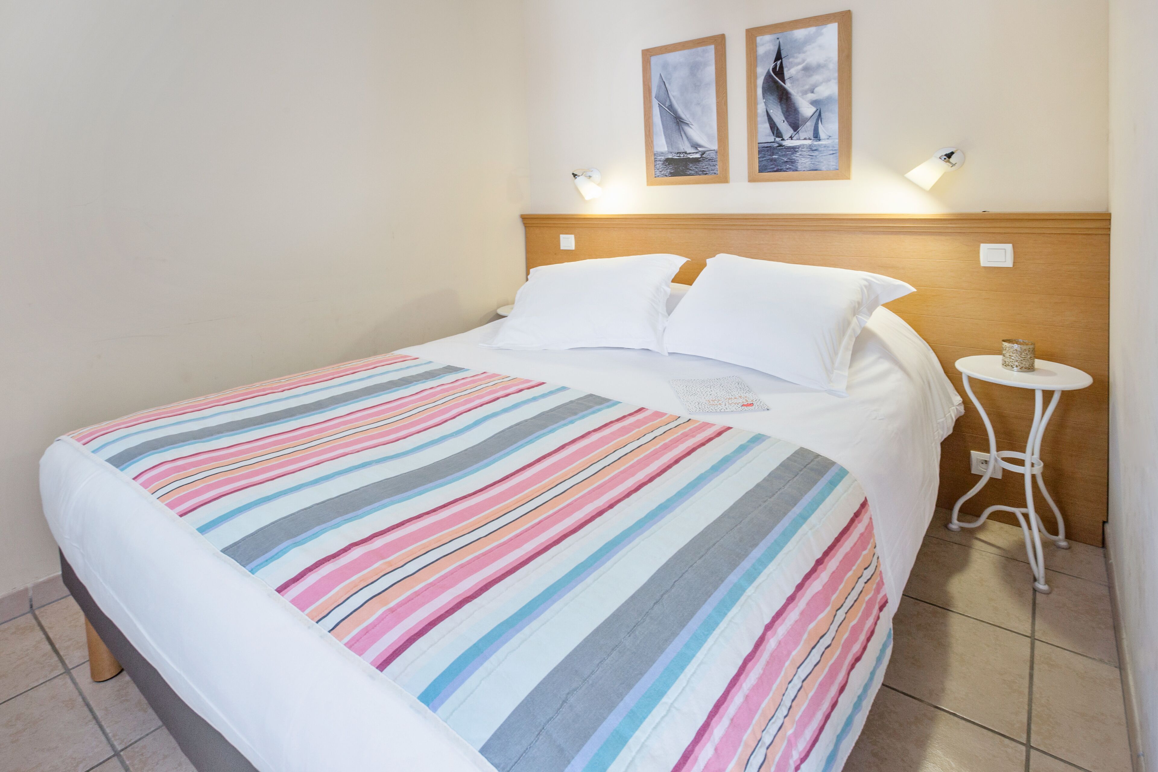 Een opgemaakt bed met een gestreept dekbed, een houten hoofdbord en twee wandlampen.