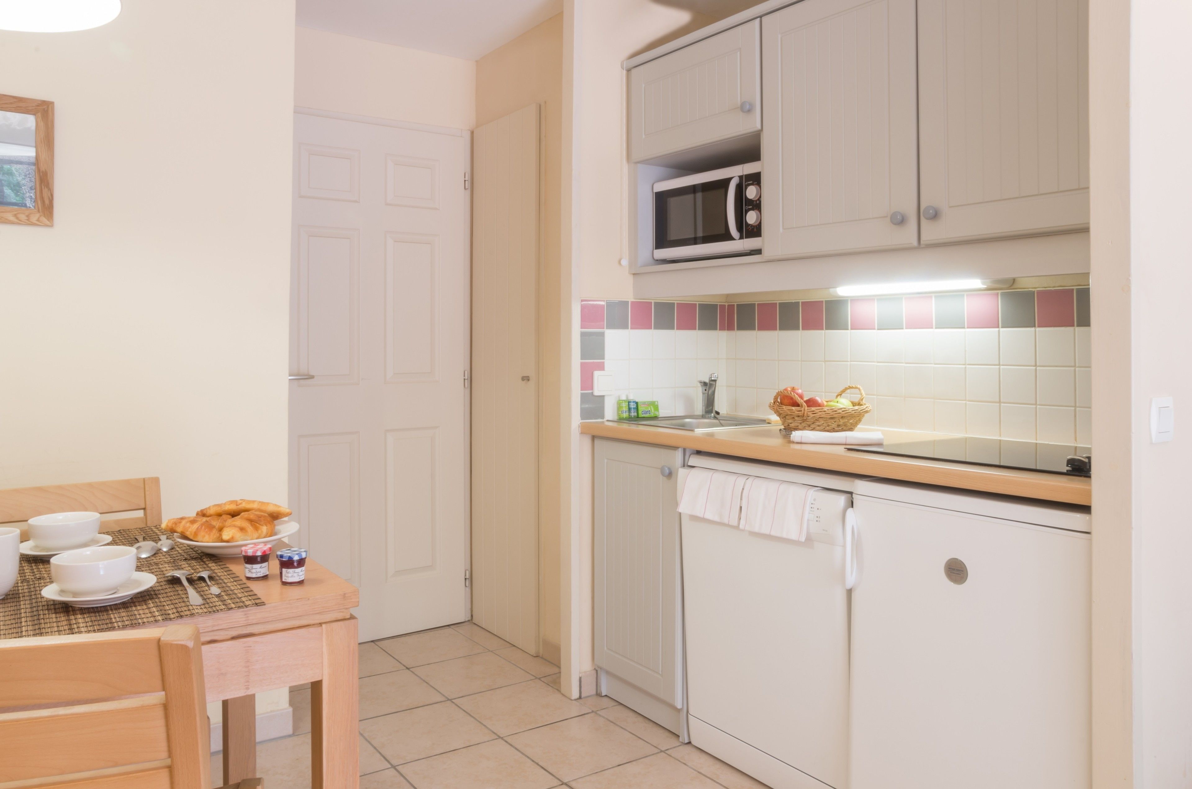 Cocina compacta con microondas, lavabo y un pequeño comedor con mesa dispuesta para el desayuno.