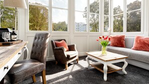 A room with large windows, a sofa, a chair, a coffee table, and a lamp.