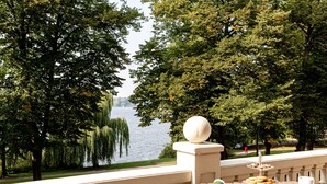 A terrace with a view of a lake, a dining table with plates, cups, and a menu.