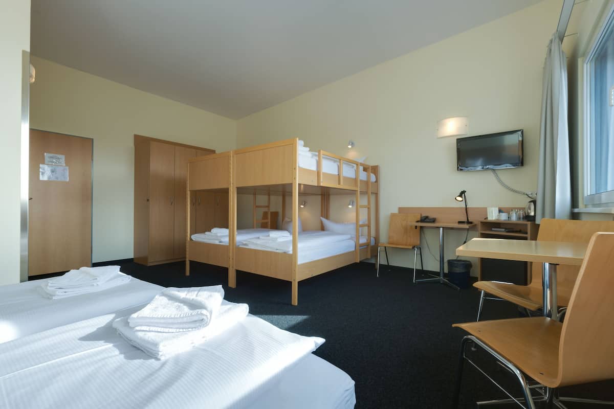 Een hotelkamer met stapelbedden, een bureau, een stoel, een televisie en een garderobe.