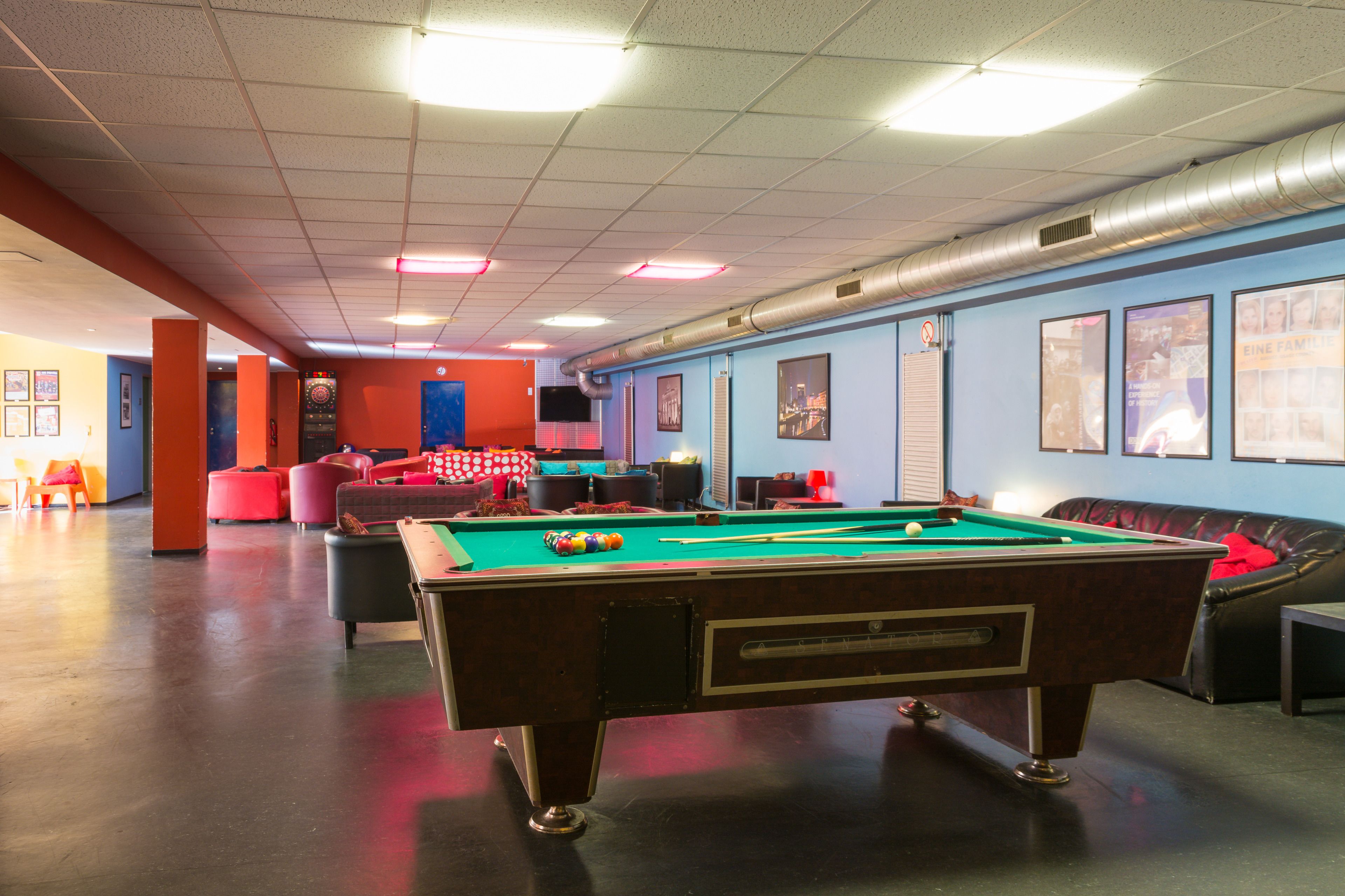 A pool table in a room with a blue wall, a red couch, and a television on the wall.
