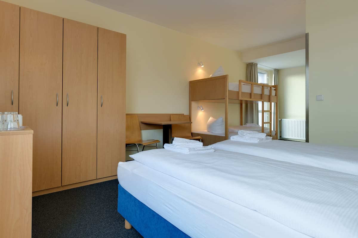 Een hotelkamer met een stapelbed, een bureau met stoel, een garderobe en een radiator.