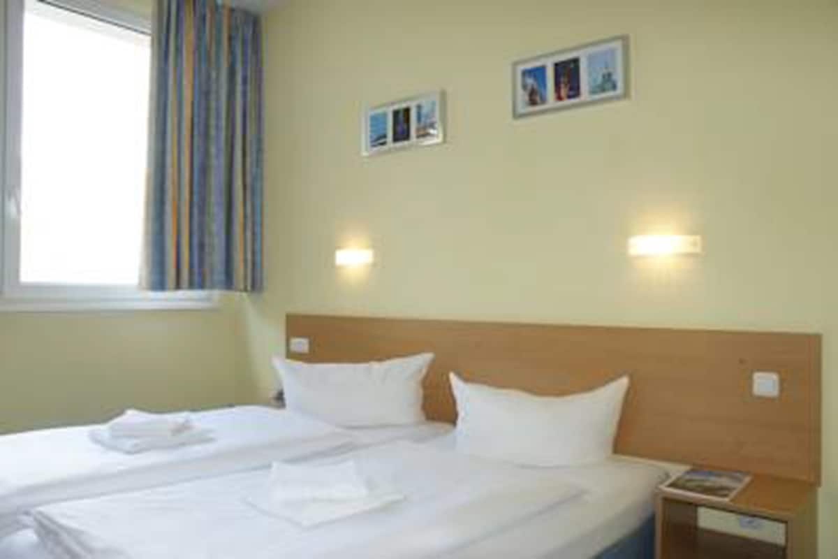 Een hotelkamer met een bed, twee nachtkastjes en een raam met gordijnen.