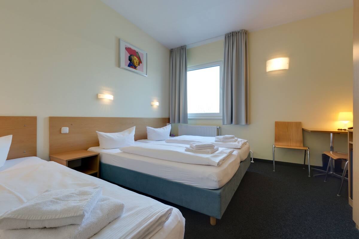 Een hotelkamer met twee bedden, een bureau, een stoel en een raam met gordijnen.