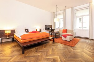 Una camera d'albergo con un letto, comodini, una TV, un divano e una grande finestra.