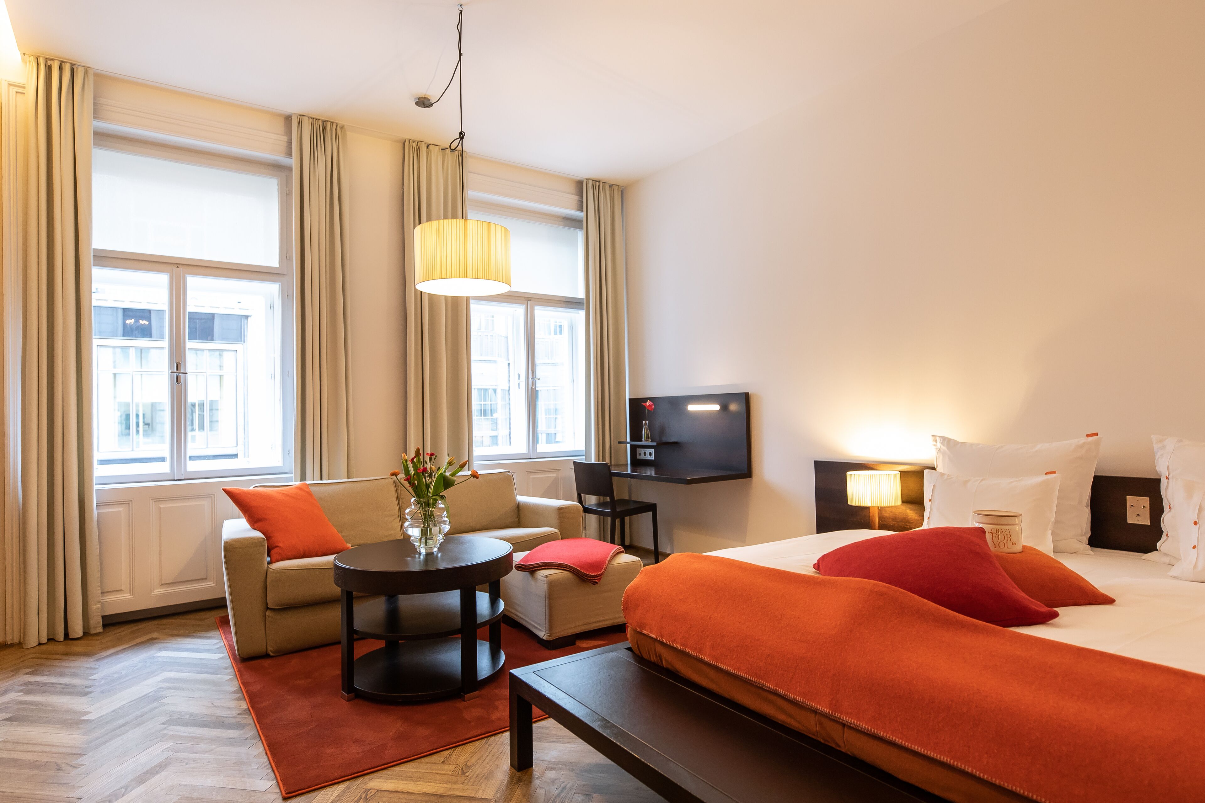 Una habitación de hotel con una cama, un sofá, una mesita, un televisor y una ventana con cortinas.