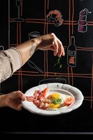 Uma mão segurando um prato com comida, uma taça de vinho e uma garrafa desenhados em um quadro-negro.