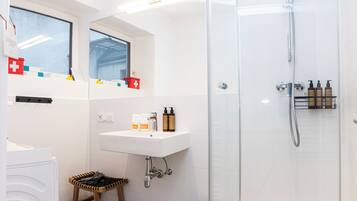 Un baño moderno con cabina de ducha de vidrio, un lavabo con artículos de aseo y un pequeño taburete.