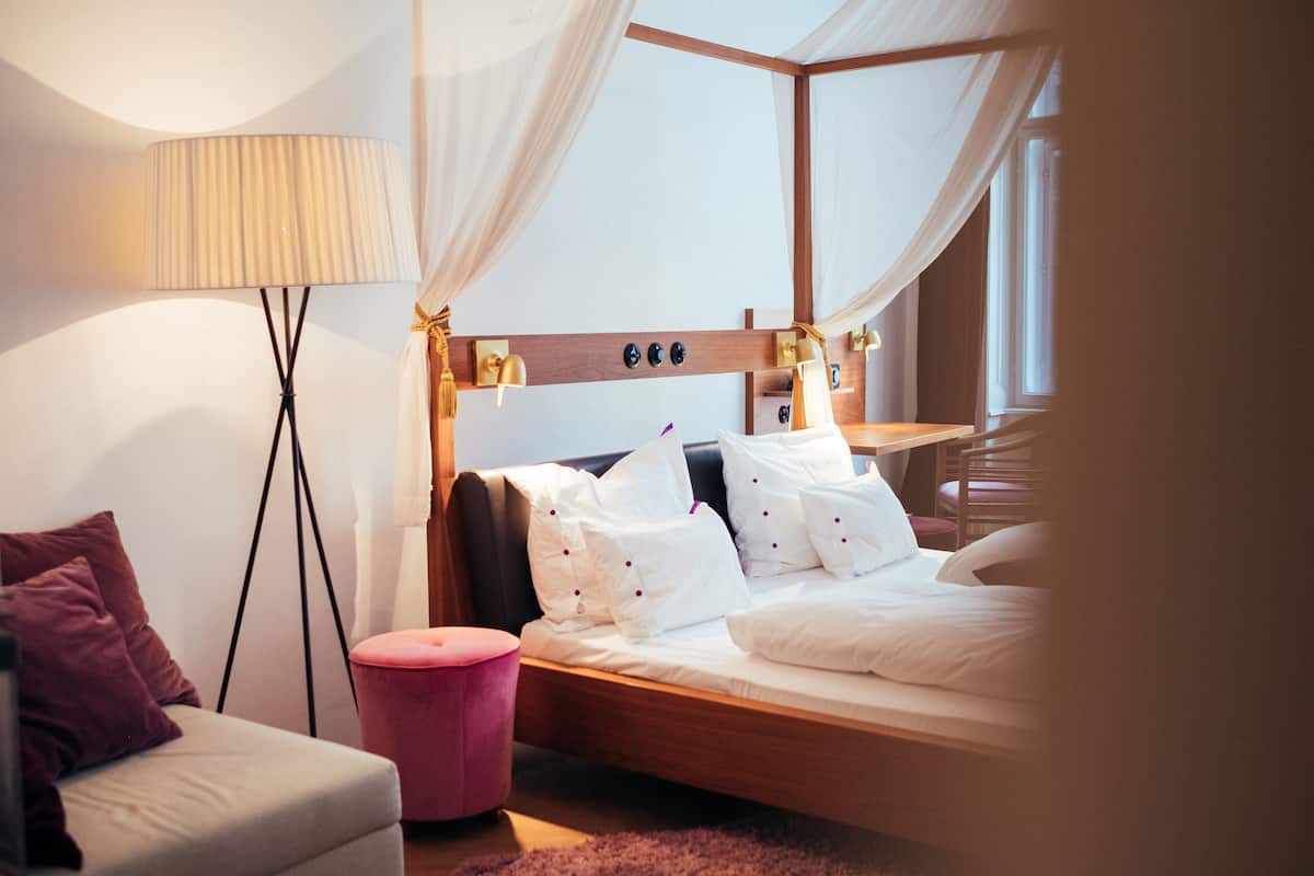 Un dormitorio moderno con cabecera de madera, ropa de cama blanca, una mesita de noche y una lámpara de pie.
