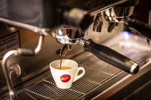 Uma máquina de café a servir expresso para uma chávena branca com logótipo vermelho.
